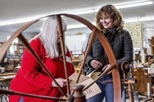 A student speaking to a craftsperson standing behind a spinning wheel