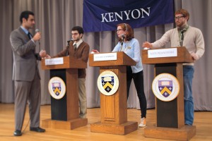 Three students behind podiums and an announcer during a quiz bowl competition