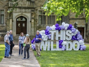 Alumni standing in front of a lighted sign which reads 'This will do' from Reunion 2024