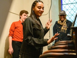 A student plays the chapel bells while two other students look on